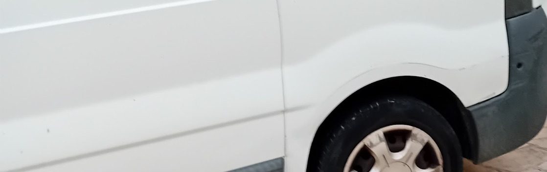 Fourgon blanc avec une roue visible et un bas de caisse gris.