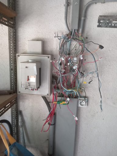 coffret dépouillé Tableau électrique avec des fils désordonnés et un disjoncteur sur un mur gris.